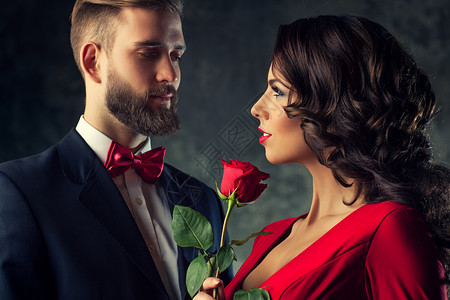 轻优雅的夫妇穿着晚礼服肖像穿红色衣服的女人抱着玫瑰看着男人专注于女人图片