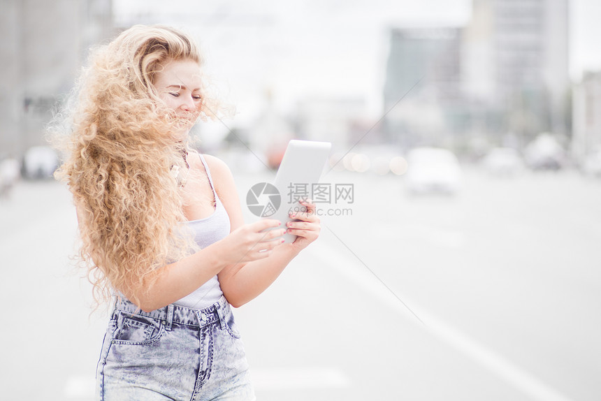 快乐的轻女人,脖子上戴着老式音乐耳机,平板电脑上上网,城市背景下摆姿势图片
