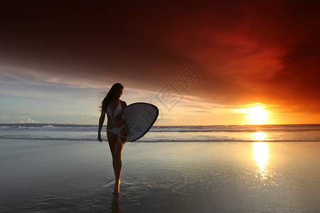 日落时海滩上的冲浪女孩日落时海滩上美丽的冲浪女孩背景图片