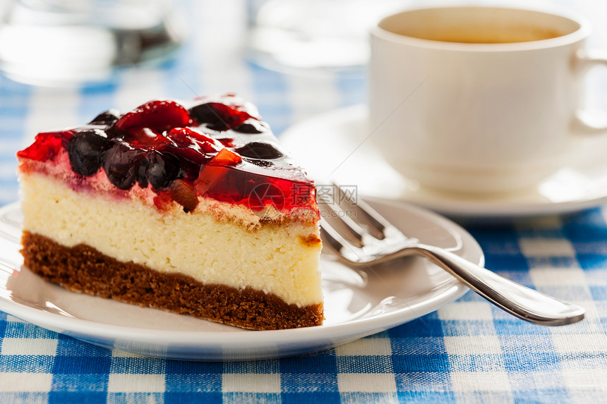 甜点背景水果奶酪蛋糕盘子与叉子咖啡杯蓝色格子桌布带叉子咖啡杯的盘子上的蛋糕图片