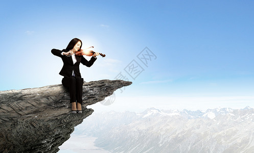 女小提琴手轻的女人坐岩石边缘拉小提琴背景图片