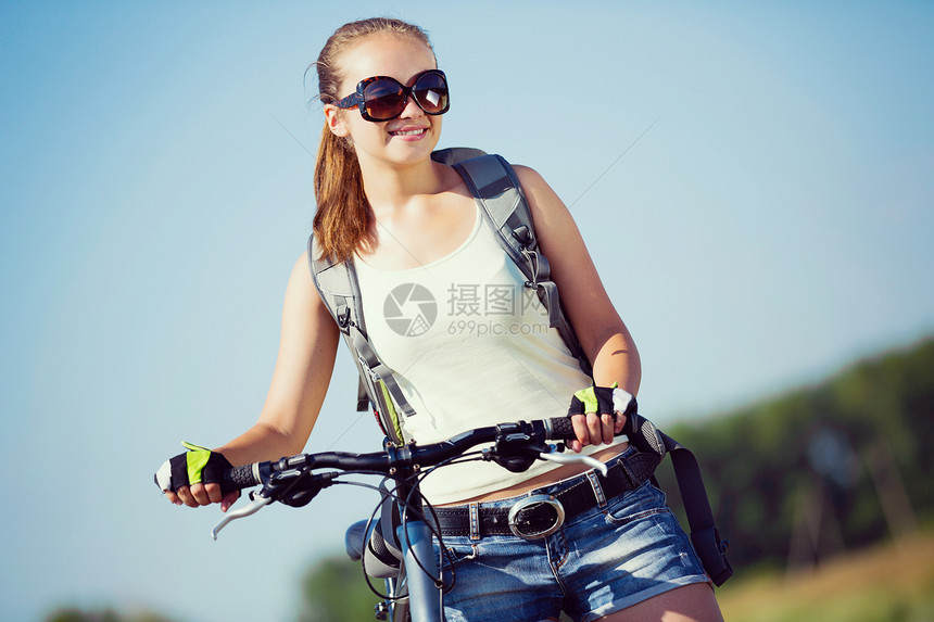 你积极的生活方式轻的运动女孩,背包骑自行车沿路边图片