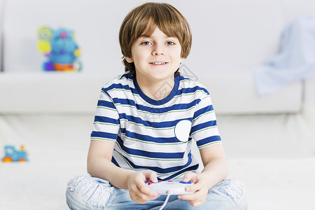 男孩坐地板上,用操纵杆敲打喜欢电子游戏背景图片