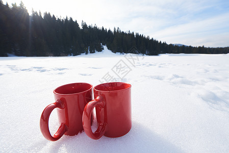 两辆红色的热茶饮料雪中,美丽的冬季阳光明媚的天,与木屋森林的背景场景高清图片素材
