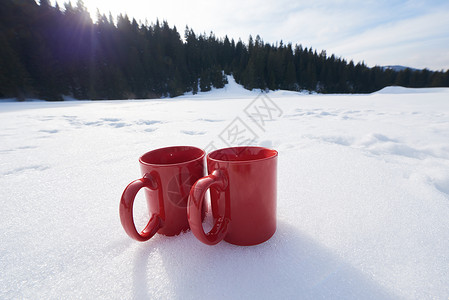 两辆红色的热茶饮料雪中,美丽的冬季阳光明媚的天,与木屋森林的背景自然的高清图片素材