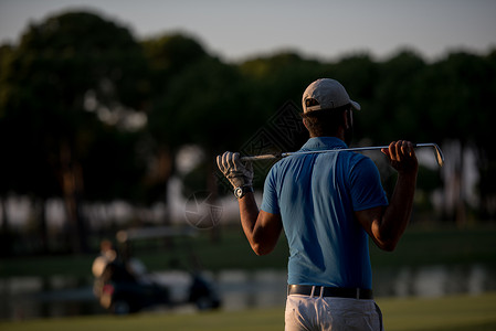 高尔夫球手后看球洞远处,英俊的中东高尔夫球员肖像后与美丽的日落背景图片