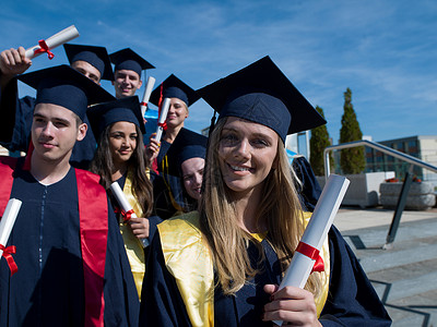 毕业日,轻的毕业生们站大学大楼前白天高清图片素材