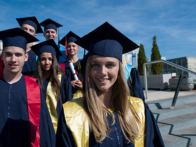 毕业日,轻的毕业生们站大学大楼前成人高清图片素材