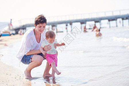 快乐的妈妈宝宝海滩上玩得开心,同时学会走路迈出步高清图片