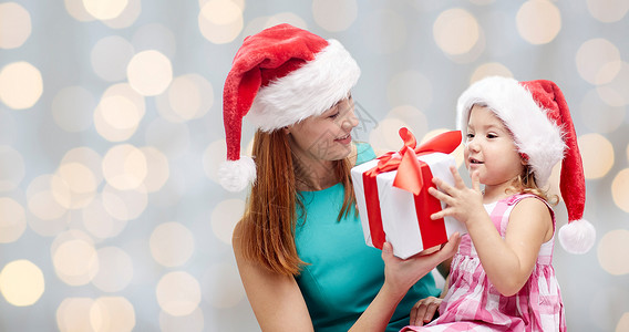 诞节,家庭,童人的快乐的母亲小女孩戴着诞帽,节日灯的背景下礼品盒背景图片
