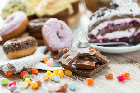 垃圾食品,糖果健康的饮食巧克力片,果冻豆,釉甜甜圈蛋糕木桌上图片