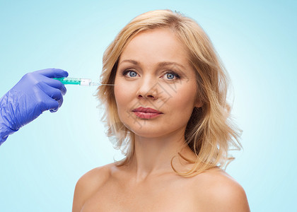 美容,抗衰容手术的中妇女的脸美容师携手手套注射器,蓝色背景下注射脸颊背景图片