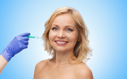 美容,抗衰容手术的微笑的中妇女的脸美容师手套与注射器,蓝色背景下注射脸颊背景图片