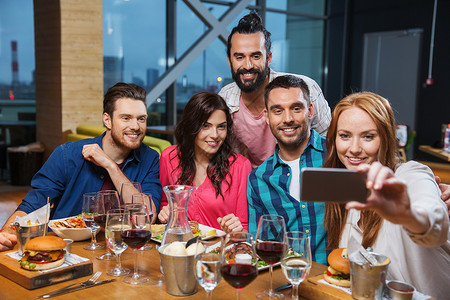 休闲,技术,友谊,人假日的快乐的朋友餐厅吃晚饭用智能手机自拍背景图片