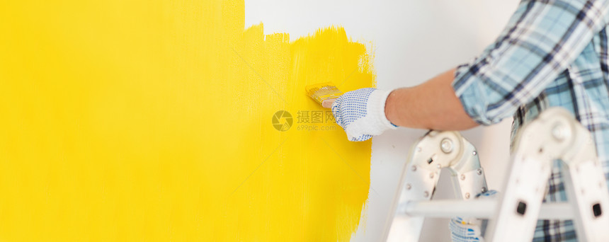 修理家庭改造的男的手手套上涂黄色油漆的墙壁把戴手套的男人关来画墙图片