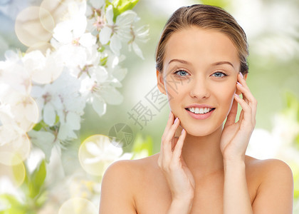 美丽,人健康的微笑的轻女人,裸露的肩膀触摸她的脸绿色的自然背景与樱花图片