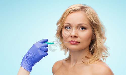 美容,抗衰容手术的女人的脸美容师携手手套与注射器制造注射嘴唇蓝色背景背景图片
