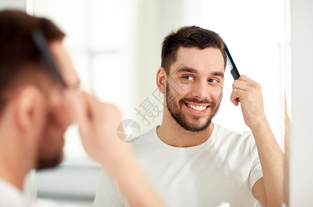 美丽,修饰人的微笑的轻人看着镜子,家里的浴室用梳子梳头图片