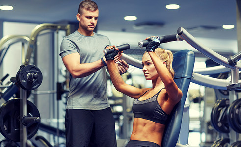 肌肉肱二运动,健身,队合作人的轻的妇女私人教练健身机上伸展肌肉背景