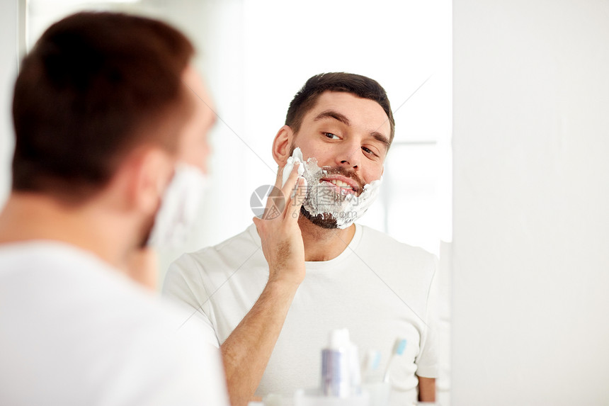 美容,卫生,剃须,美容人们的微笑的轻人看着镜子,家里的浴室里用剃须泡沫图片