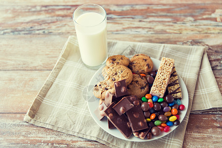 垃圾食品,糖果健康的饮食糖果,巧克力,穆斯利饼干与牛奶璃盘子图片
