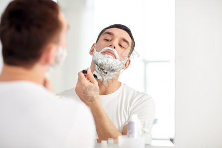 美容,卫生,剃须,美容人的轻人看镜子剃须胡须与手动剃须刀刀片家里浴室图片