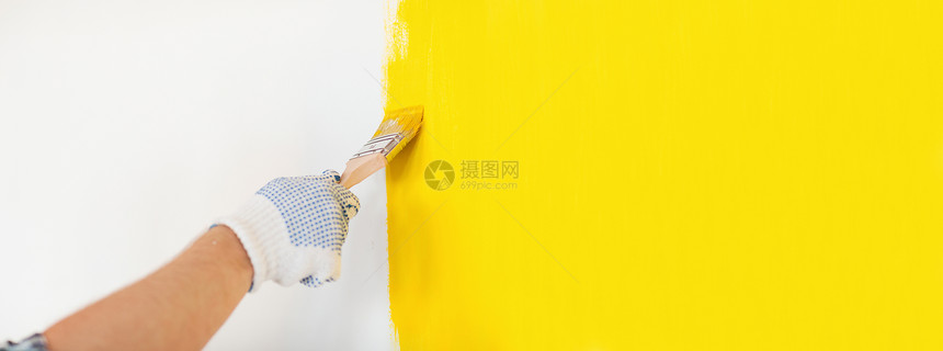 修理家庭改造的男的手手套上涂黄色油漆的墙壁把戴手套的男人关来画墙图片