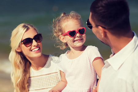 家庭,假期,收养人的快乐的男人,女人戴太阳镜的小女孩夏天的海滩上交谈图片