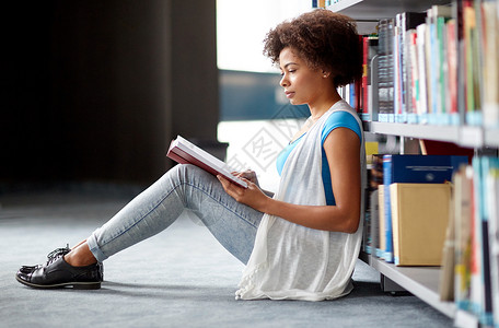 教育,高中,大学,学人的非裔美国学生女孩阅读书籍坐图书馆的地板上图片
