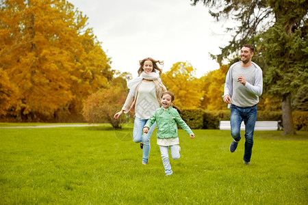 家庭亲子休闲人的快乐的母亲父亲小女孩秋天的城市公园里跑步玩接球游戏图片