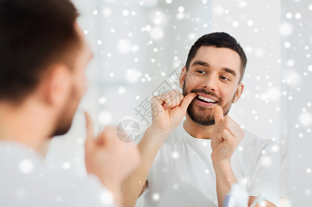 保健,牙科卫生,人美容微笑的轻人用牙线清洁牙齿,并家里的浴室看镜子雪背景图片