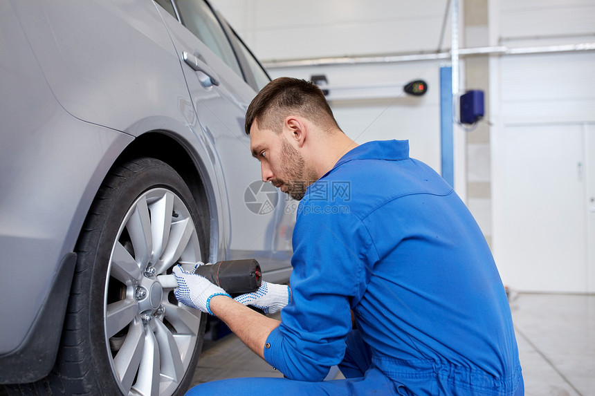 汽车服务,维修,维护人的汽车技工与电动螺丝刀更换轮胎车间图片