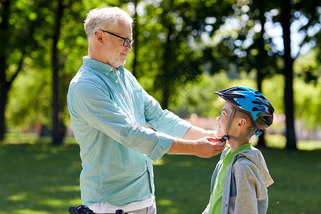家庭,世代,安全人的快乐的祖父帮助男孩夏季公园的自行车头盔图片