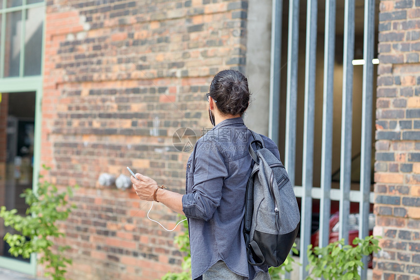 人技术旅行旅游带背包智能手机耳机的人沿着城市街道行走,听音乐图片