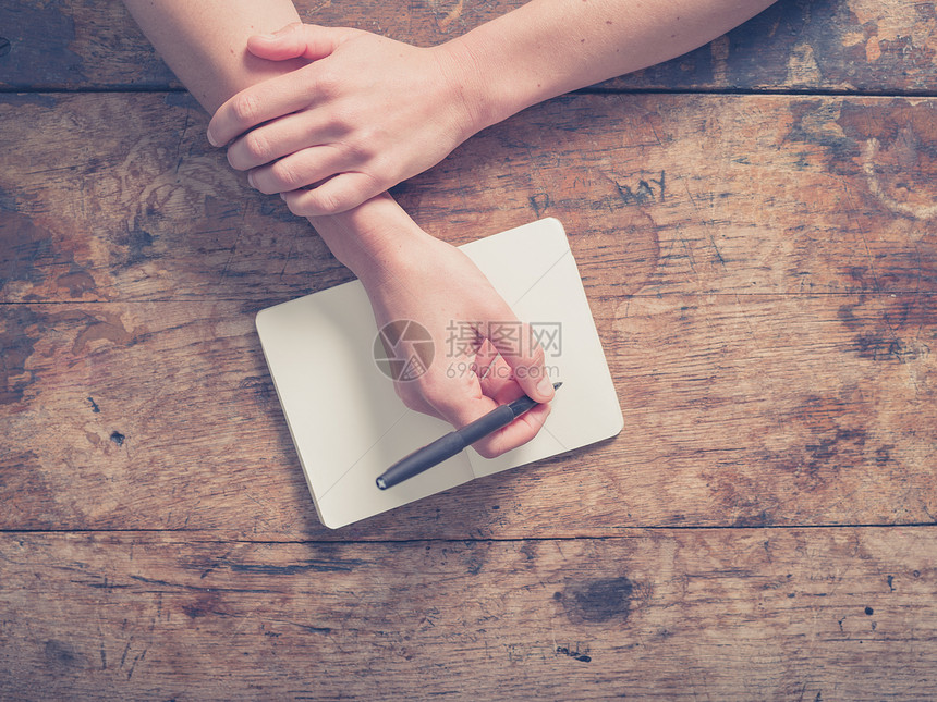 靠近个轻女人的手,因为她正个小记事本个木制的桌子上写字图片