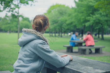 屈膝个轻的女人独自坐公园里的张桌子上,正野餐背景