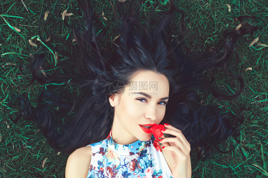 户外时尚照片,美丽的轻女士草地上,嘴里草莓图片