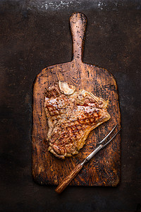 优秀的烤烤t骨牛排与肉叉老化的木制切割板上的深锈金属背景,顶部视图图片