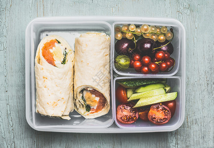 包心鱼卷健康的午餐盒与素食玉米饼包装,切碎的蔬菜水果木制背景,顶部视图背景
