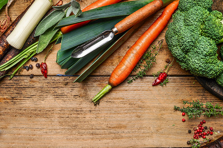 新鲜蔬菜烹饪与剥皮机木制背景,顶部视图,边界健康食品素食烹饪图片