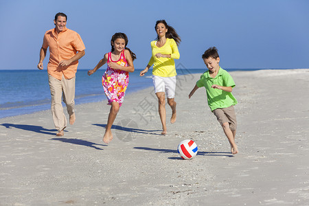 个幸福的家庭,母亲,父亲两个孩子,儿子女儿,阳光明媚的沙滩上踢足球足球图片