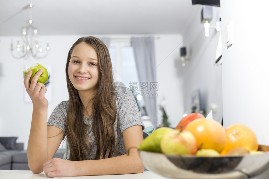 微笑的女孩坐家里的桌子上着苹果的肖像图片