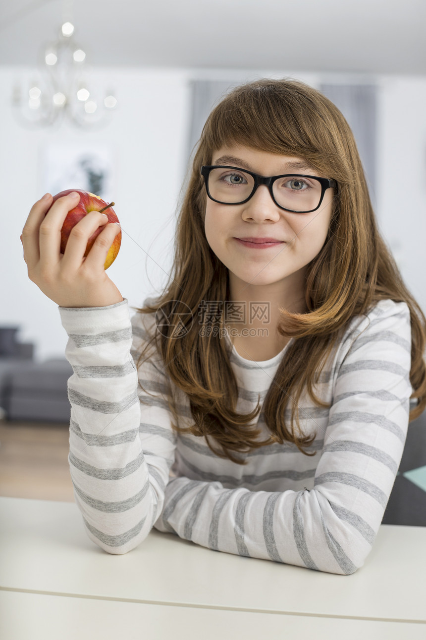 轻女孩坐家里的桌子上着苹果的肖像图片