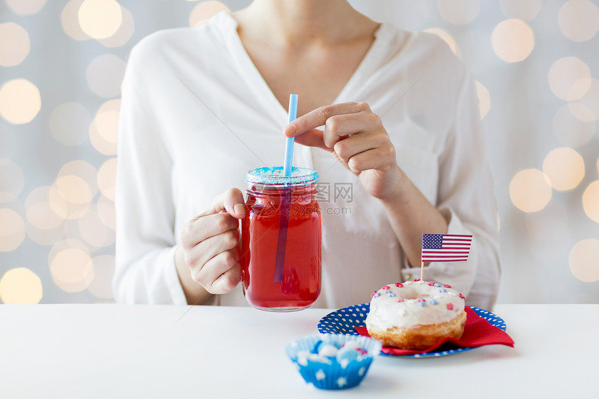 独立日,庆祝,主义节日的妇女吃釉甜甜甜圈,喝果汁大璃梅森罐杯子,并庆祝7月4日家聚会图片