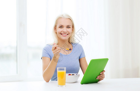 健康的饮食,饮食人的微笑的轻妇女与平板电脑家里吃早餐图片