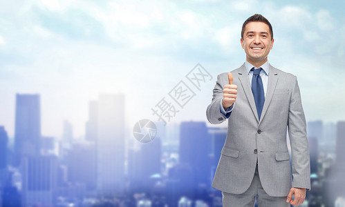 商业人手势成功穿着西装的快乐微笑的商人城市背景上竖大拇指图片