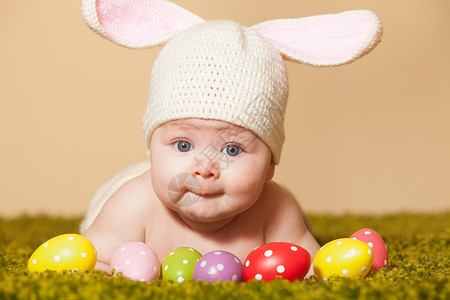帽子中兔子三个月的婴儿躺他的肚子上,就像复活节兔子草地上带着鸡蛋复活节小兔子背景