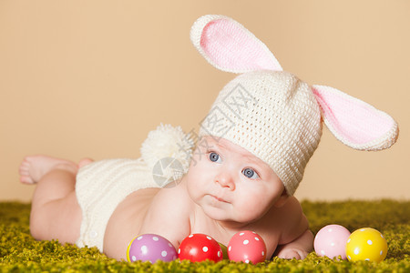 帽子中兔子三个月的婴儿躺他的肚子上,就像复活节兔子草地上带着鸡蛋复活节小兔子背景