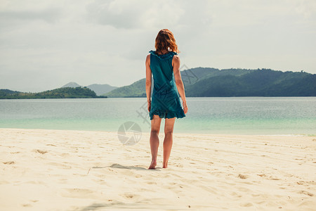 一个年轻穿着蓝色连衣裙的轻女人正热带海滩上散步图片