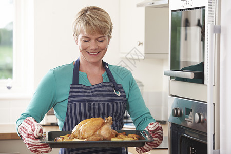 厨房里的女人着烤鸡的托盘烤箱高清图片素材
